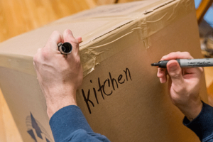 a person providing packing services writes "kitchen" on a box ready for moving