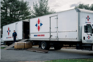 a mover stands between two Hingham Moving Services box trucks after a customer learned about Hingham Moving Services