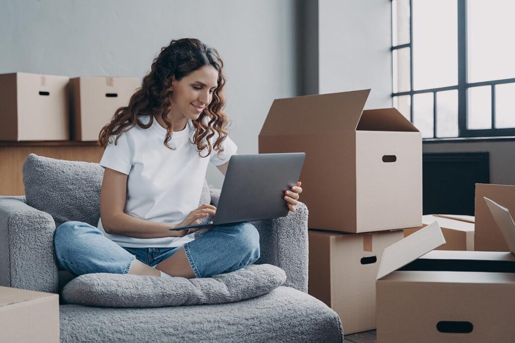 Woman sitting on comfortable chair surrounded by boxes using her laptop to find answers to the question why choose local moving services