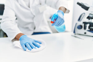 person wearing gloves spraying cleaning solution on countertop for a clean lab