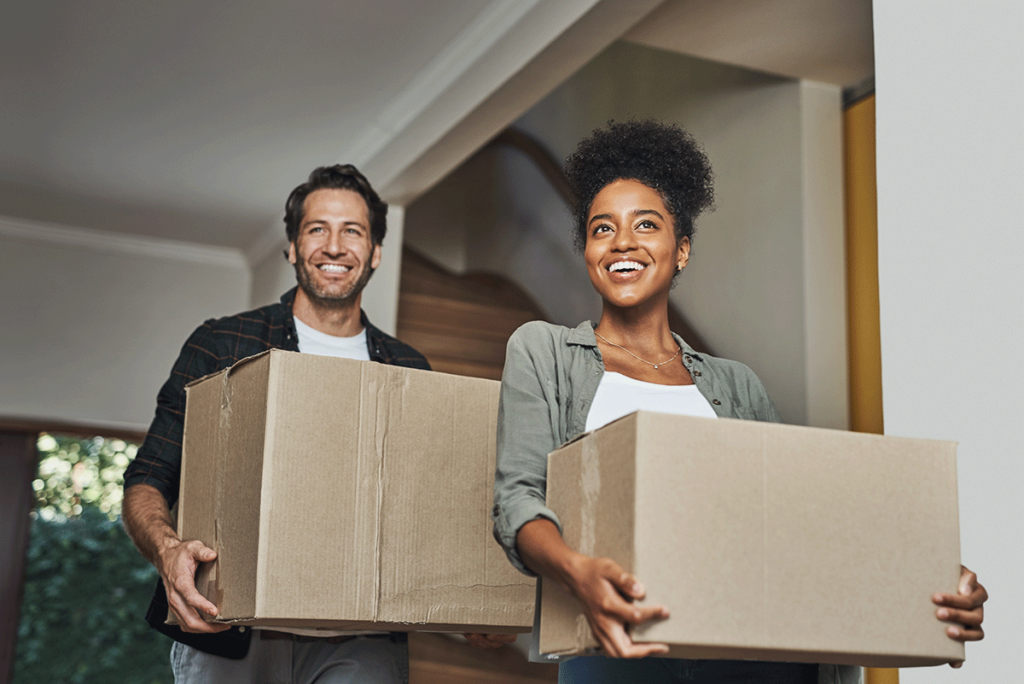 smiling couple carrying boxes while moving to durham nc